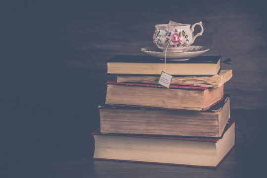 Książki w stosie, na czubku widać filiżankę z herbatą